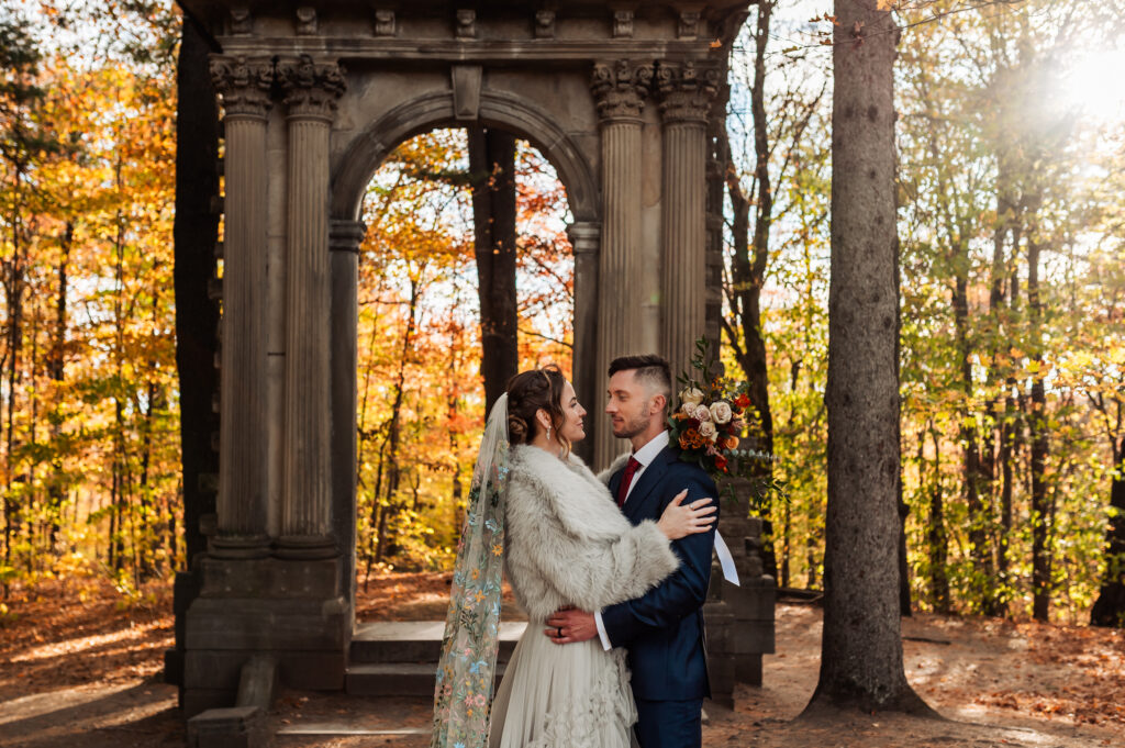 Bride and groom standing together under stone arch during fall wedding portraits in Ottawa